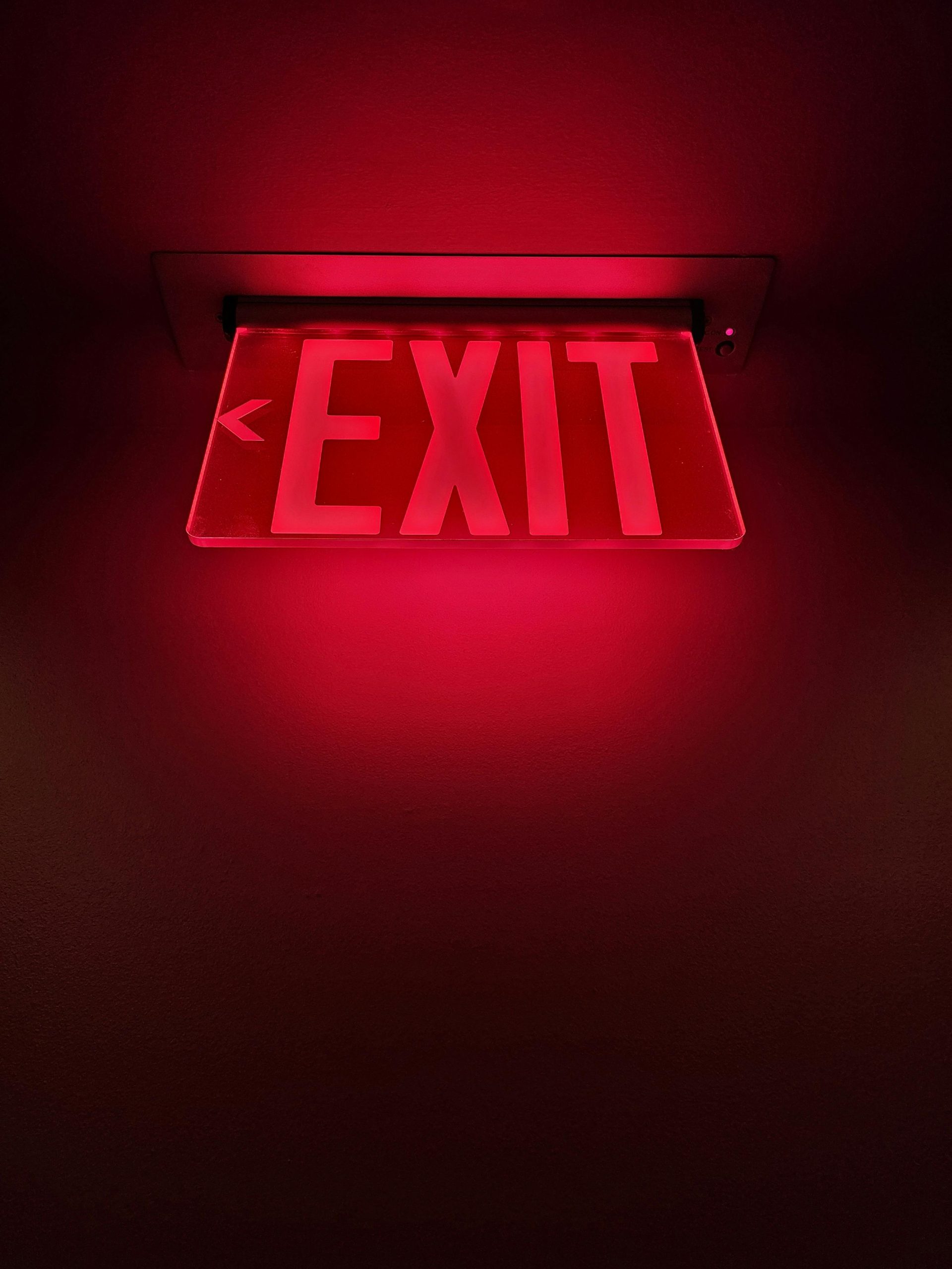 Dramatic close-up of a glowing red exit sign inside a building, perfect for emergency themes.