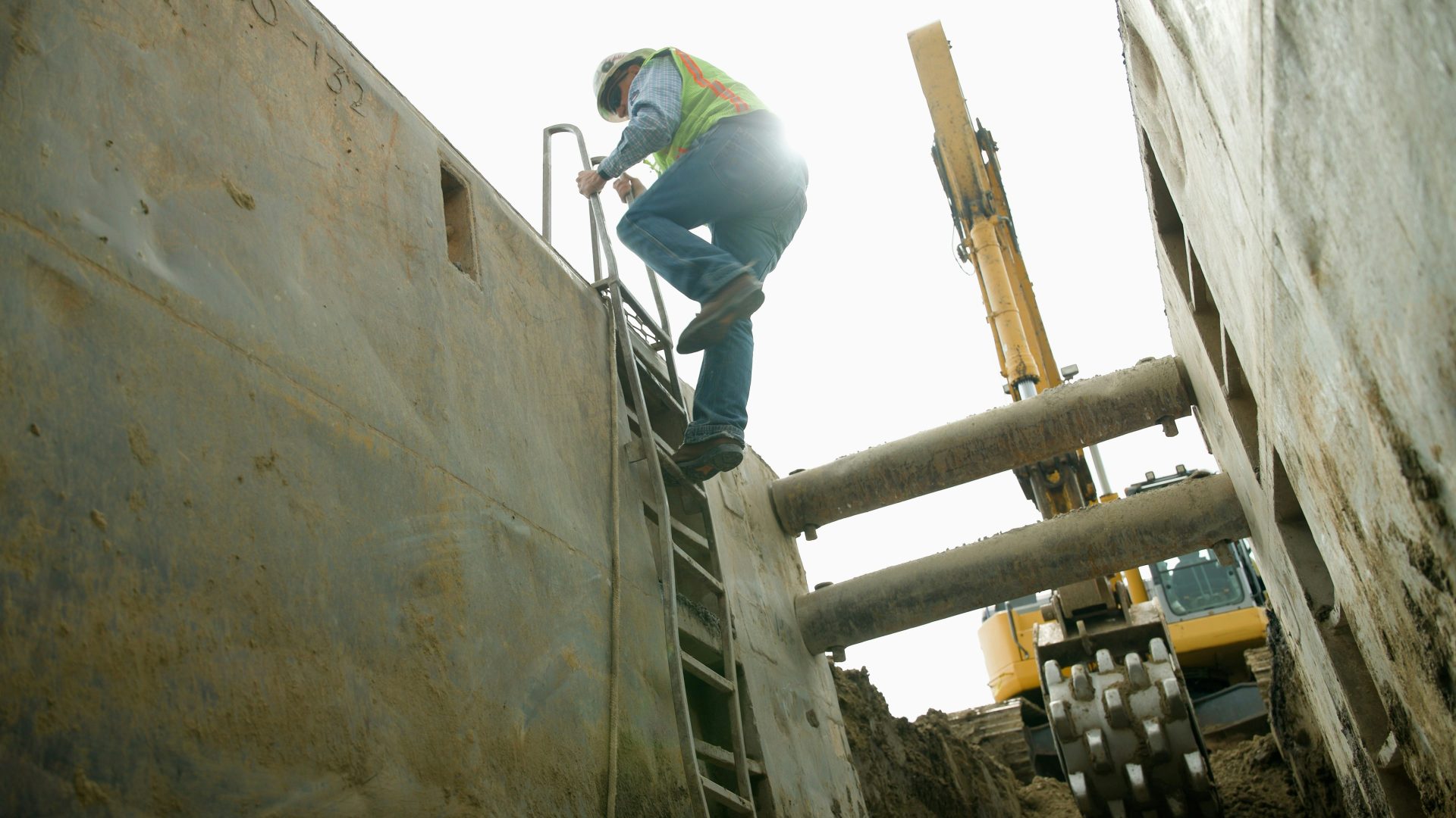 Construction worker climbs out of a deep trench.